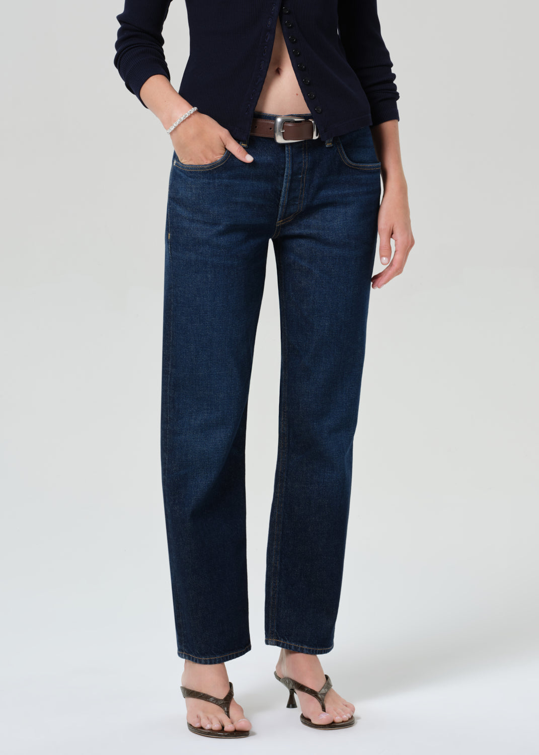 Person wearing a navy cardigan and dark blue jeans on a grey background