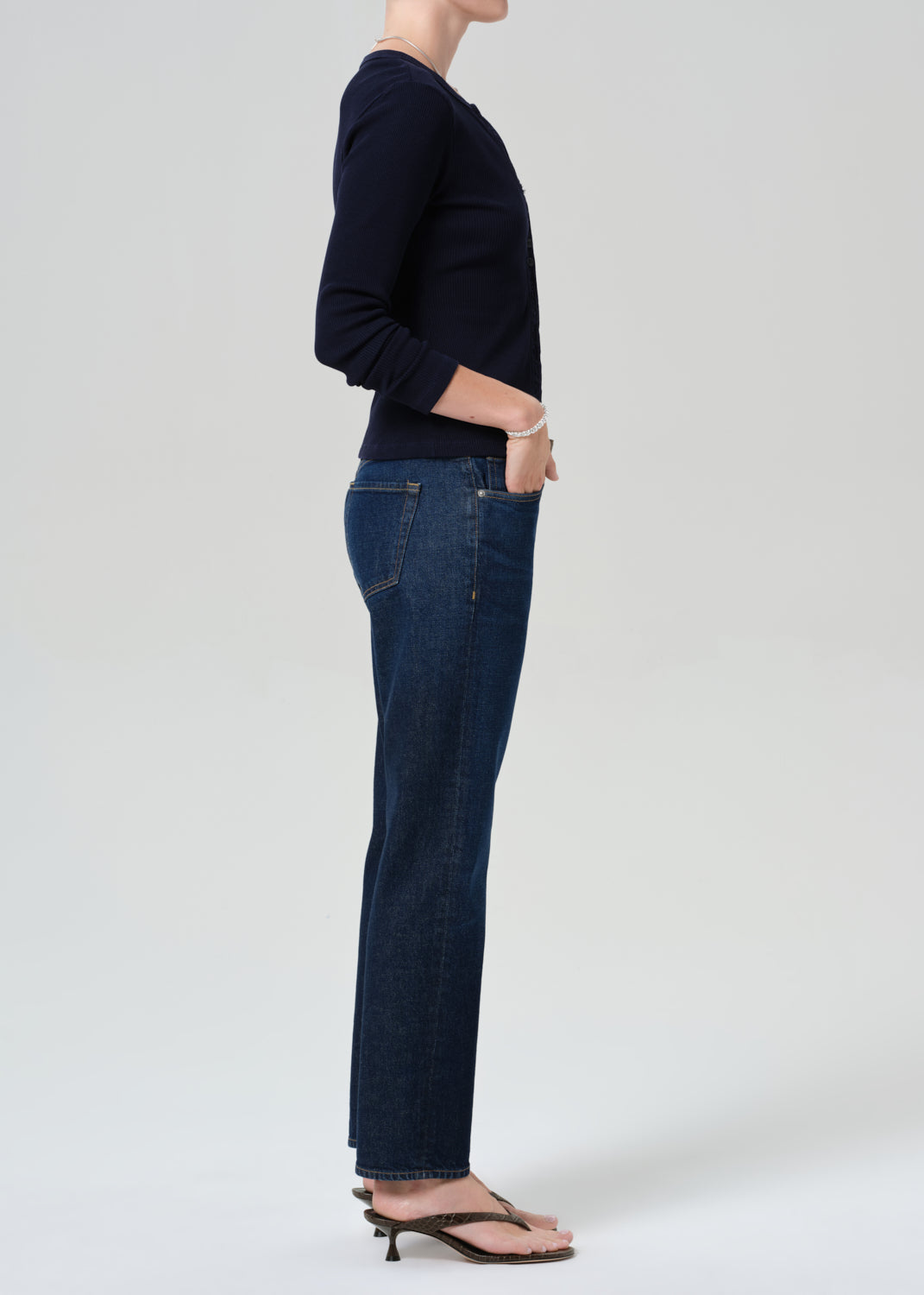 Person wearing a navy cardigan and dark blue jeans on a grey background