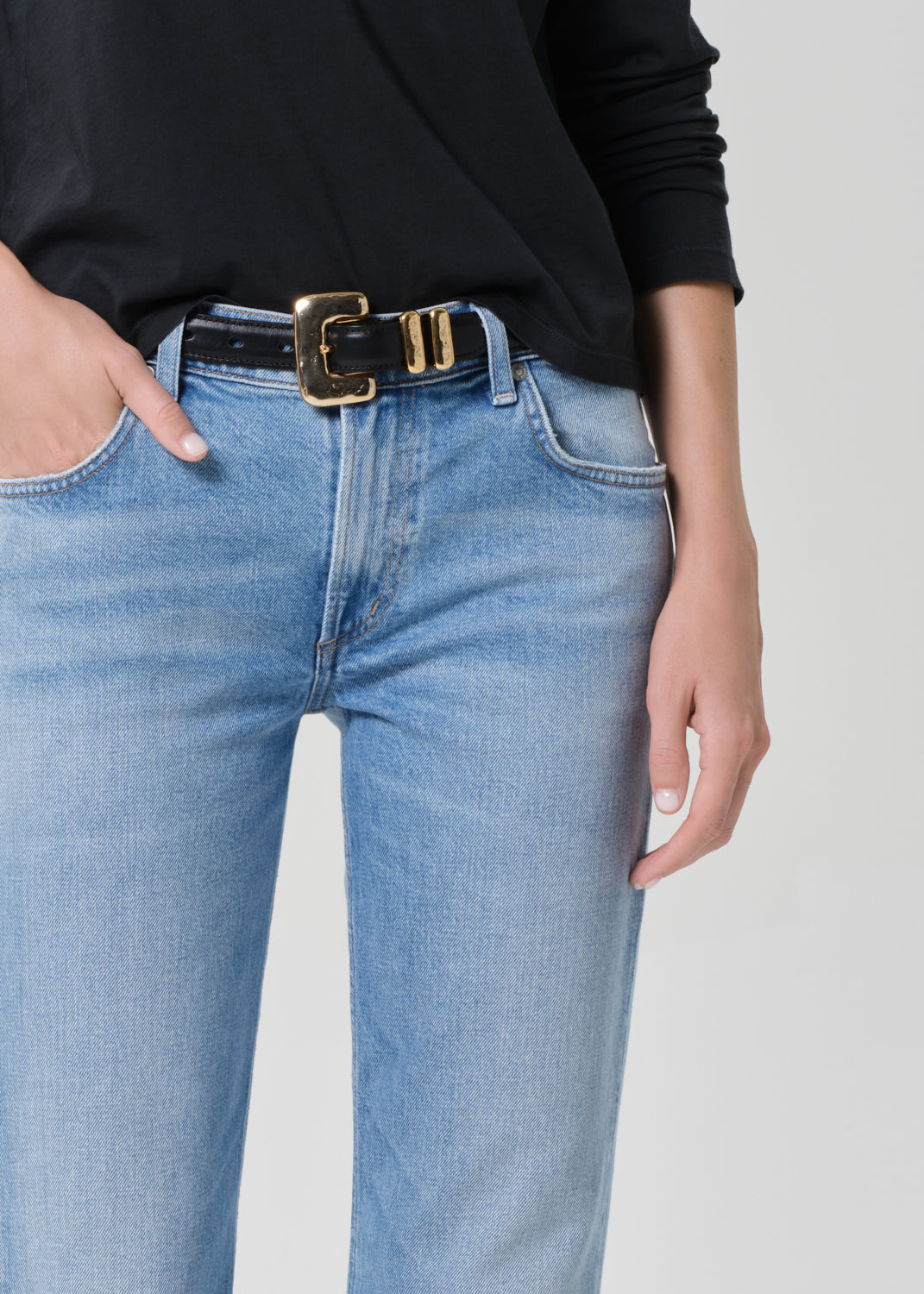 Person wearing a black long-sleeve shirt and light blue jeans on a grey background