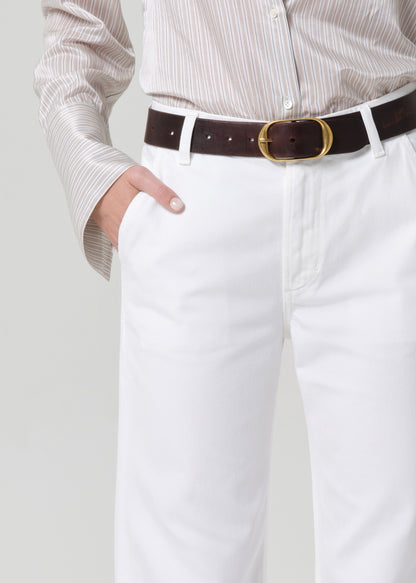 Person wearing a light-colored shirt and white jeans with a black belt on a plain background