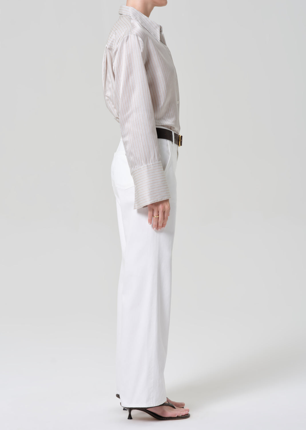 Person wearing a light-colored shirt and white jeans with a black belt on a plain background