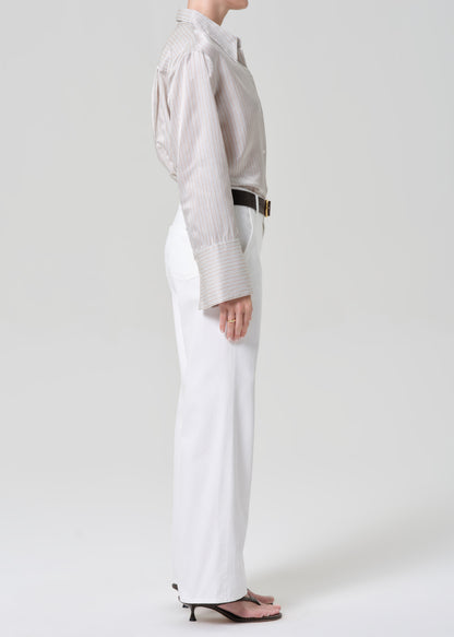 Person wearing a light-colored shirt and white jeans with a black belt on a plain background