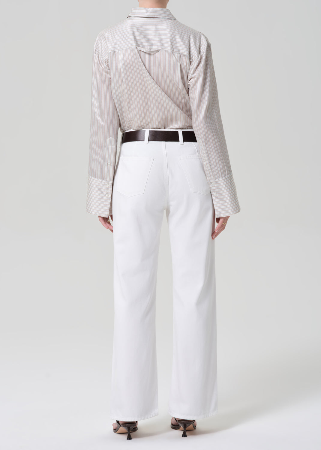 Person wearing a light-colored shirt and white jeans with a black belt on a plain background