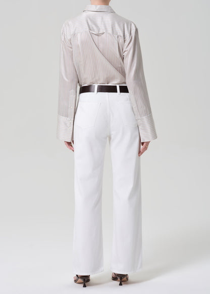 Person wearing a light-colored shirt and white jeans with a black belt on a plain background