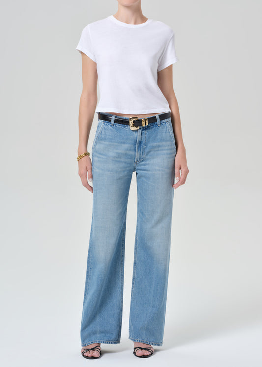 Person wearing a white t-shirt and light blue jeans on a plain background