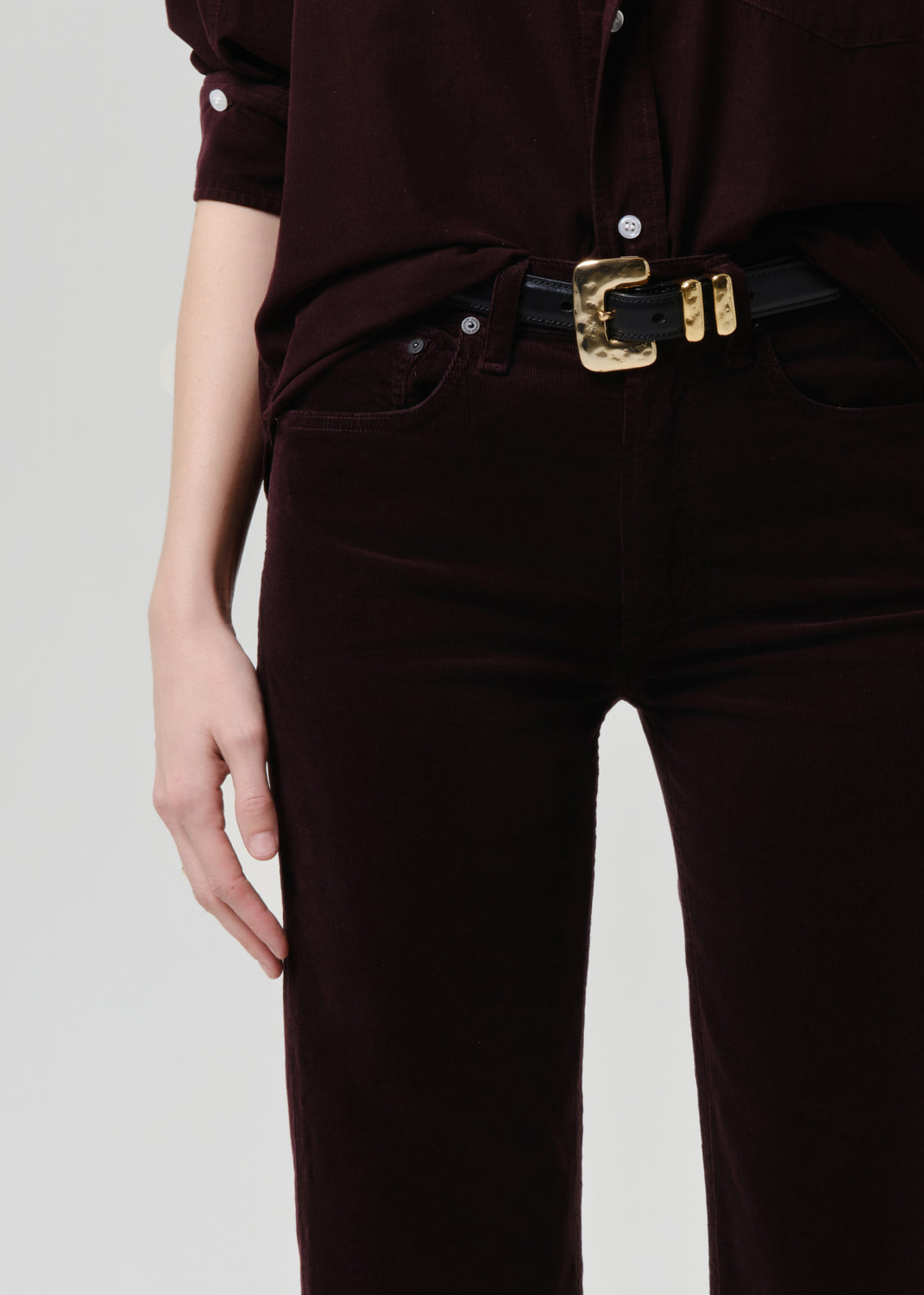 Person wearing a dark brown shirt and pants with a gold belt buckle on a grey background