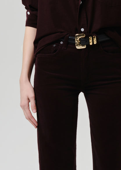 Person wearing a dark brown shirt and pants with a gold belt buckle on a grey background