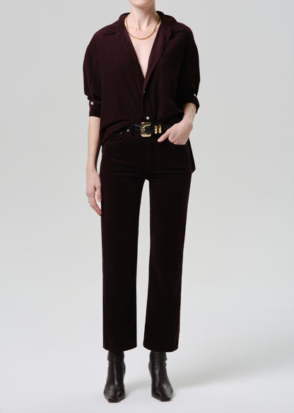 Person wearing a dark brown outfit with a belt and boots on a grey background