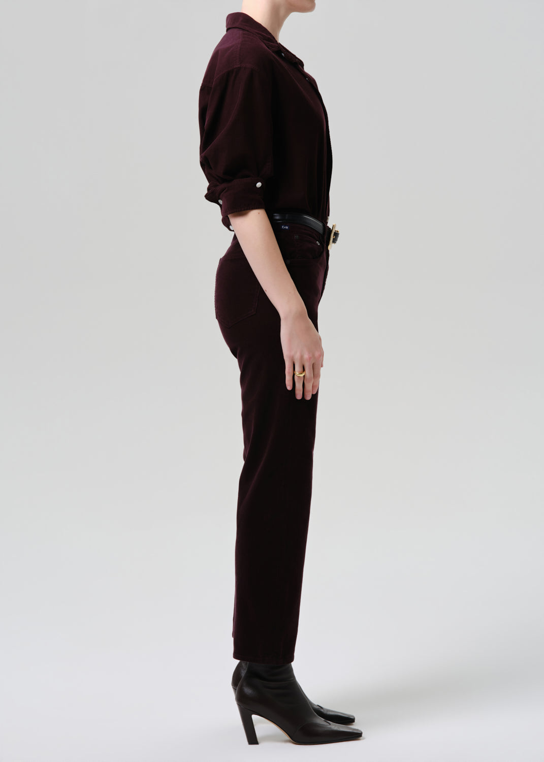 Person wearing a dark brown outfit with high heels on a grey background
