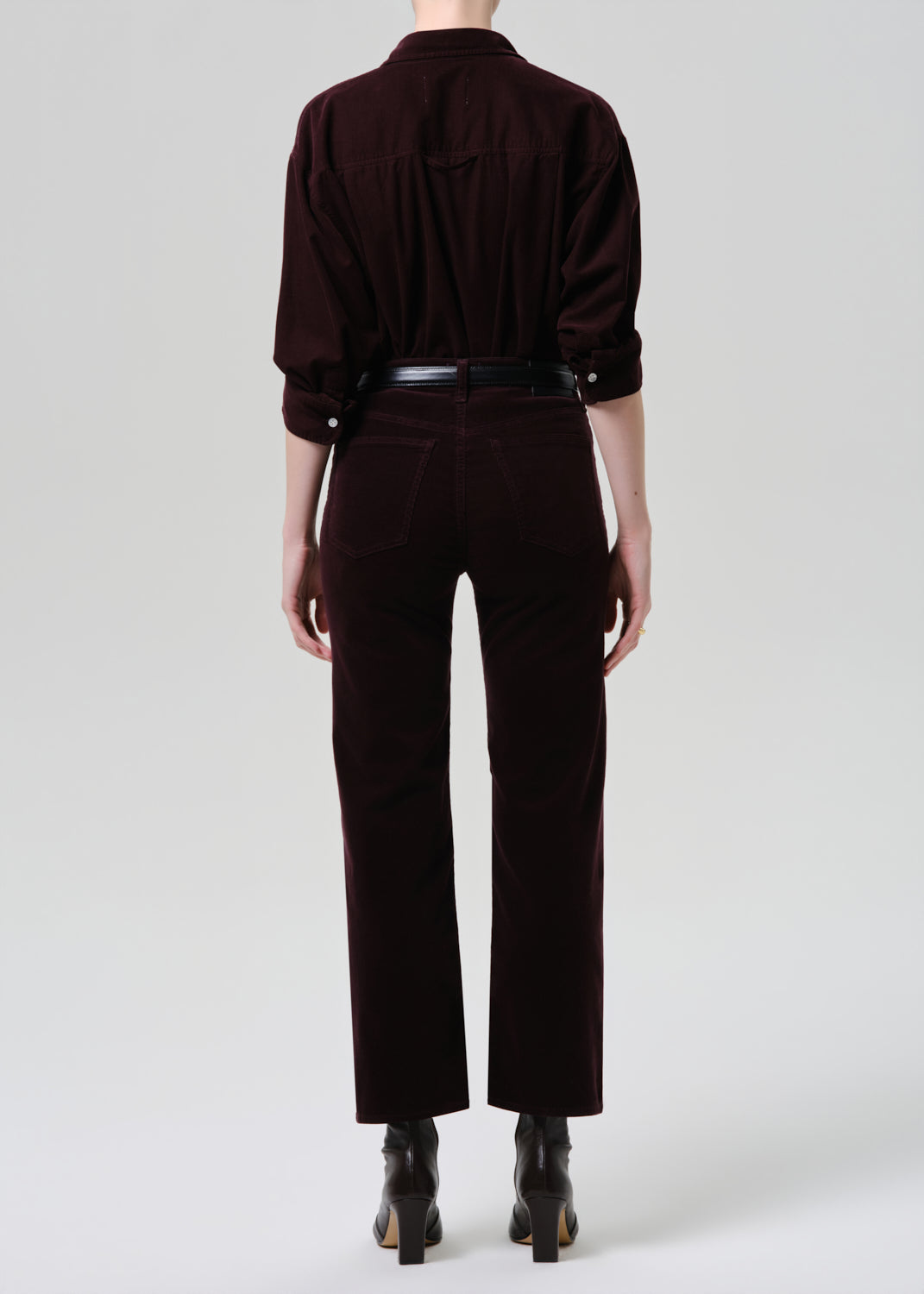 Person wearing a dark brown outfit with a shirt and pants on a grey background