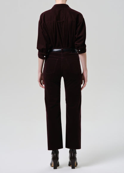 Person wearing a dark brown outfit with a shirt and pants on a grey background