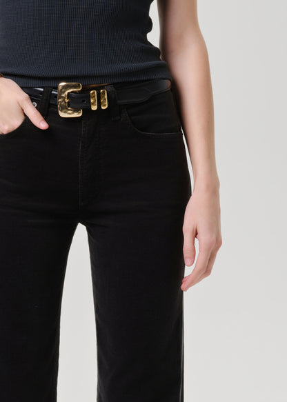 Person wearing black pants with a gold belt buckle on a grey background