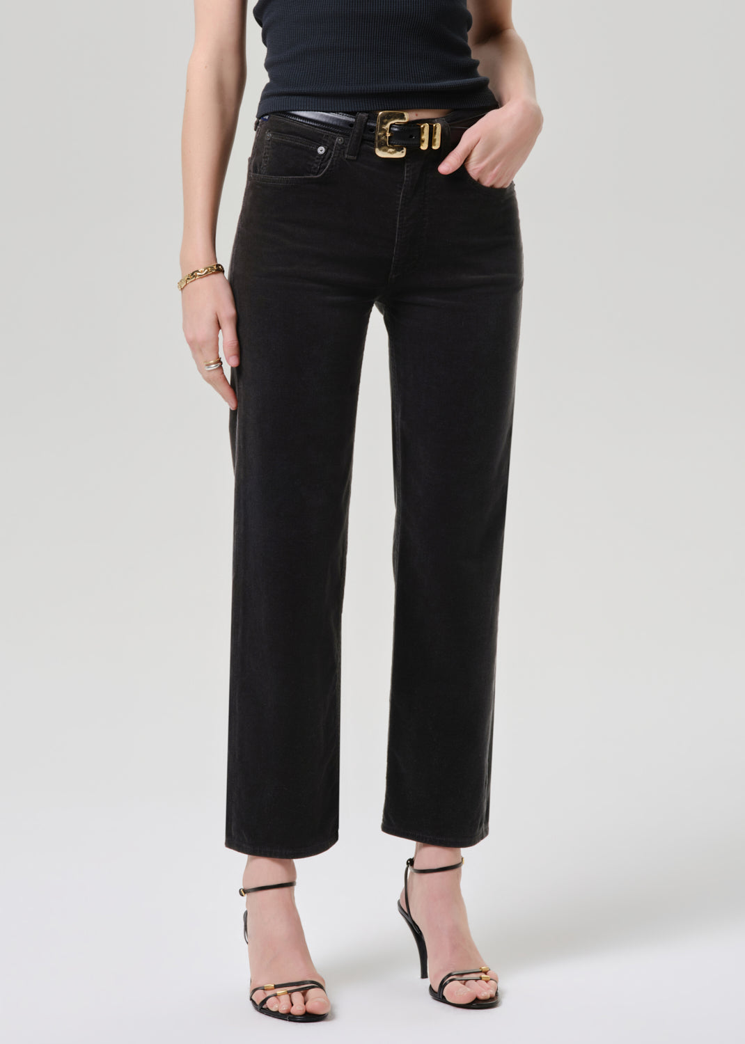 Person wearing black straight leg cropped jeans with a black short sleeve fitted top and black heels, front cropped view on a grey background.