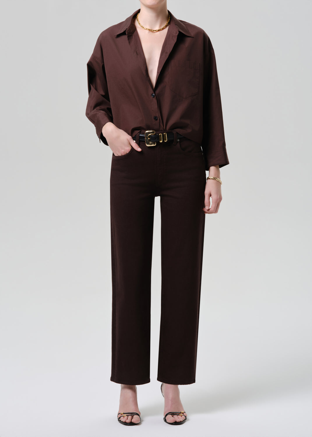 Person wearing a brown outfit with a belt on a grey background