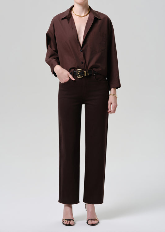 Person wearing a brown outfit with a belt on a grey background