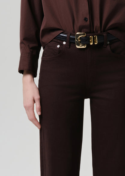 Person wearing a brown shirt and pants with a black belt on a grey background