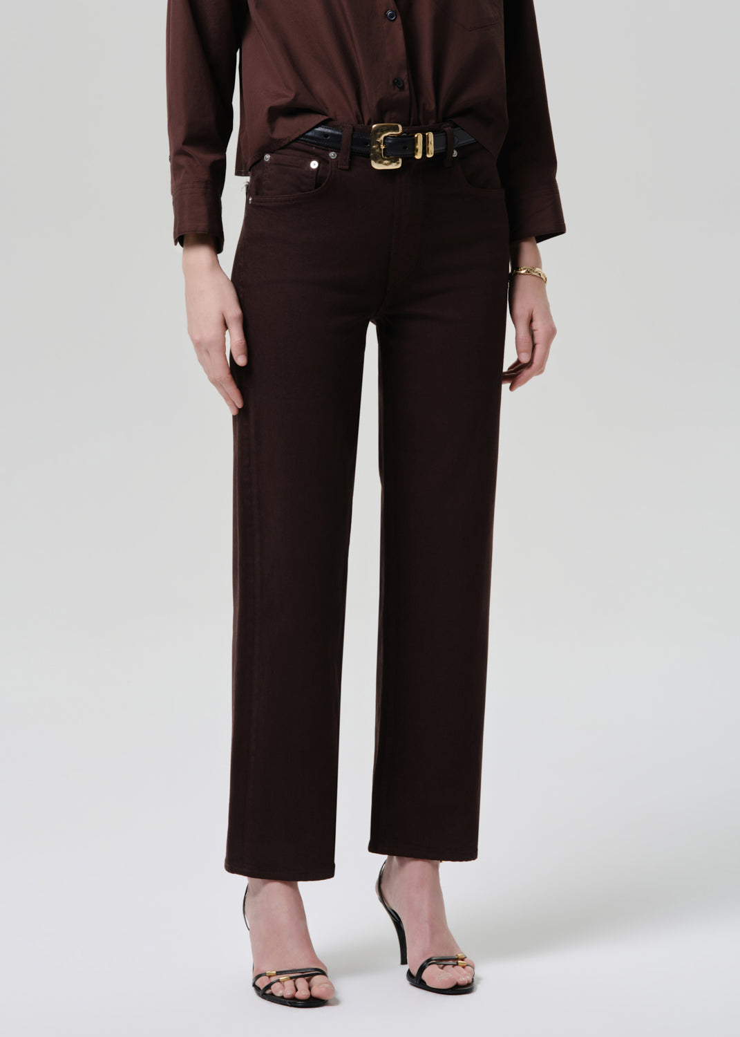 Person wearing a brown outfit with a belt on a grey background
