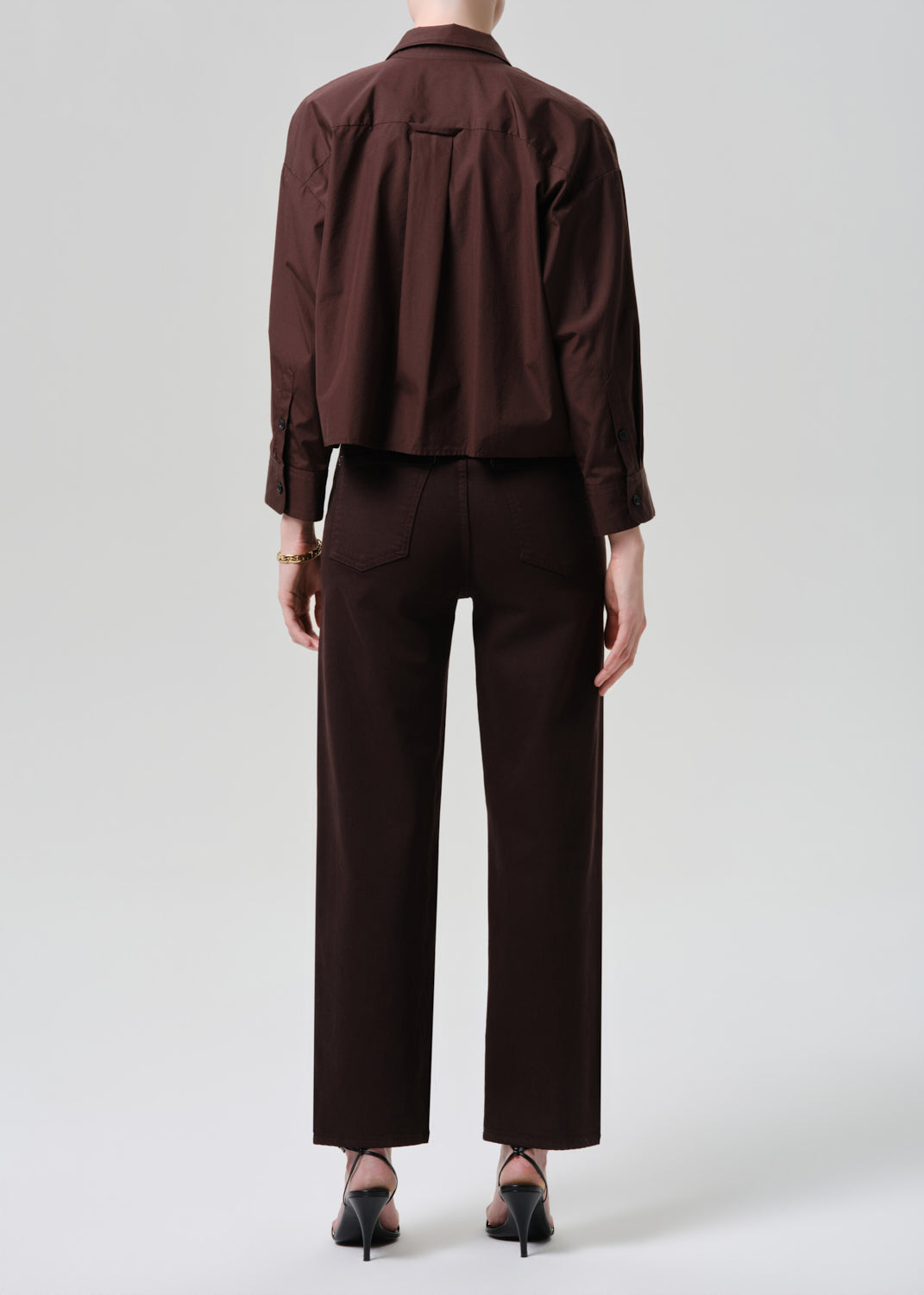 Person wearing a brown shirt and pants on a grey background