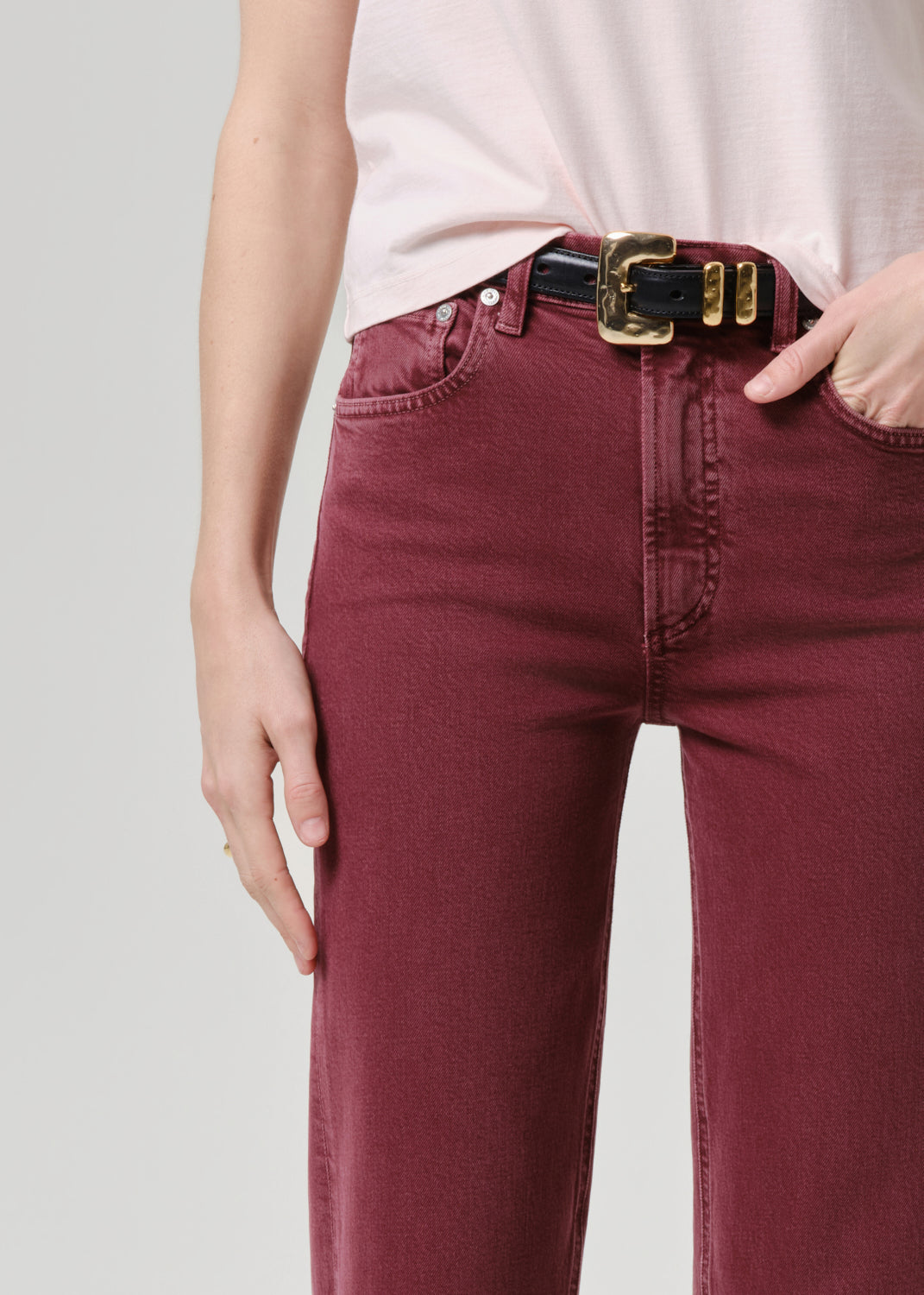 Maroon jeans with a gold belt on a grey background