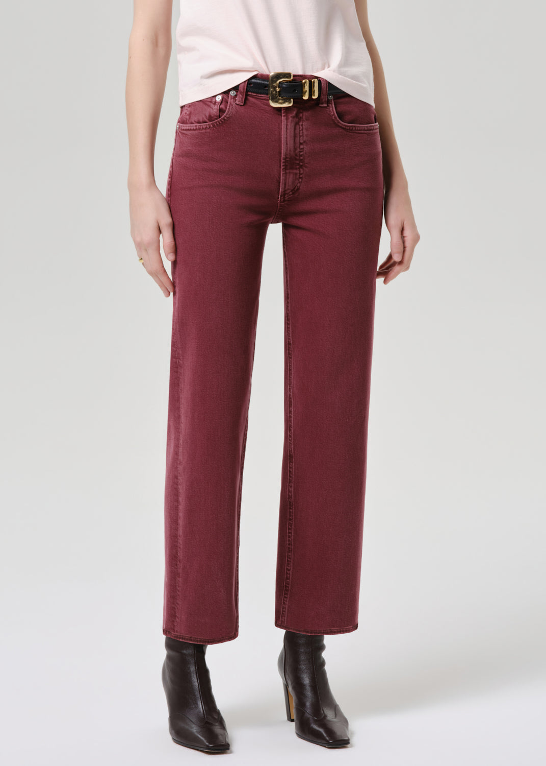 Person wearing maroon pants with a white shirt and black boots on a grey background