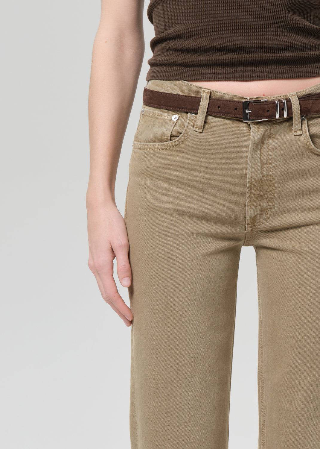 Person wearing a brown top and beige jeans on a grey background