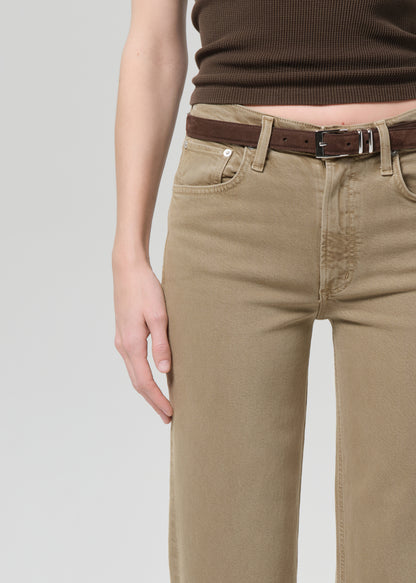 Person wearing a brown top and beige jeans on a grey background