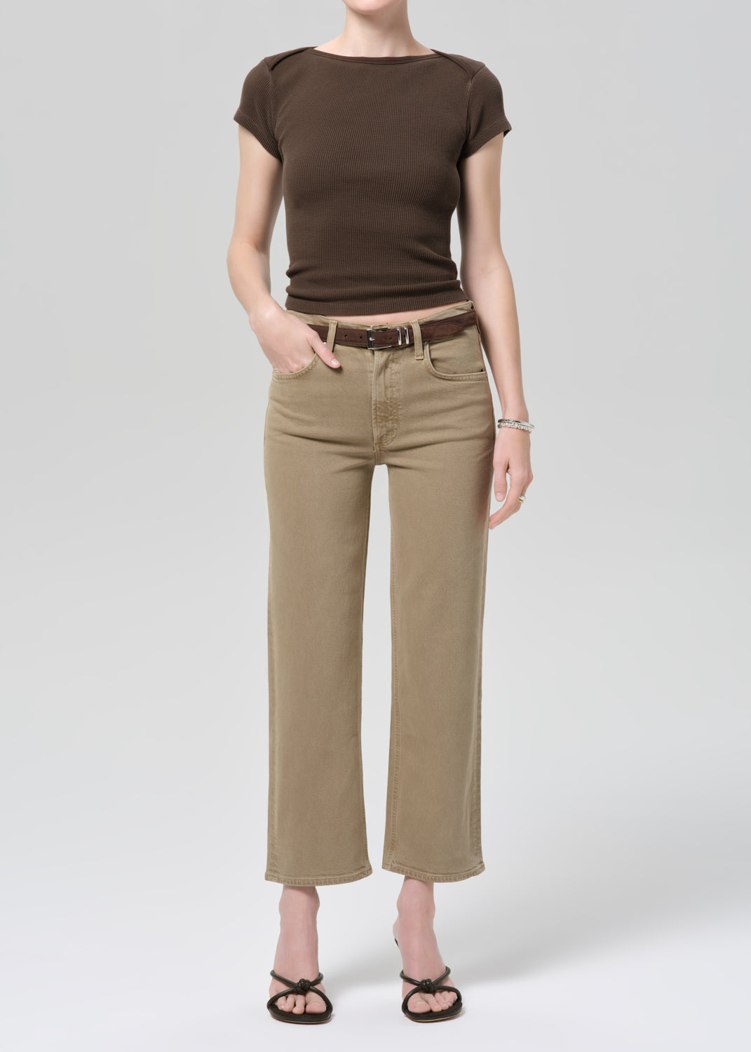 Person wearing a brown top and beige jeans on a grey background
