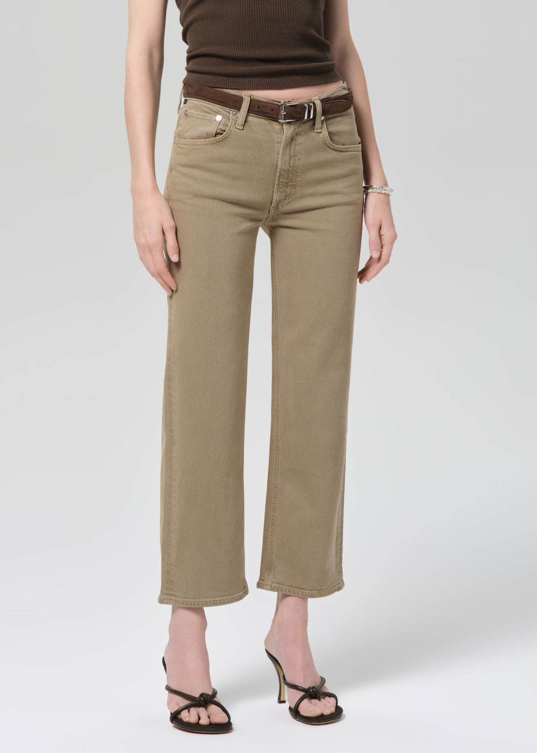 Person wearing a brown top and beige jeans on a grey background