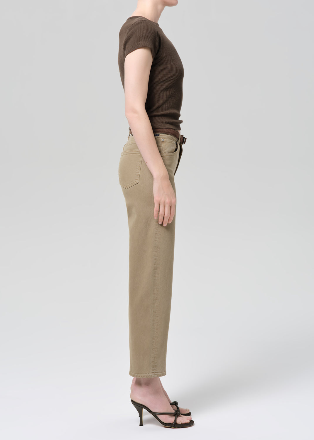 Person wearing a brown top and beige jeans on a grey background