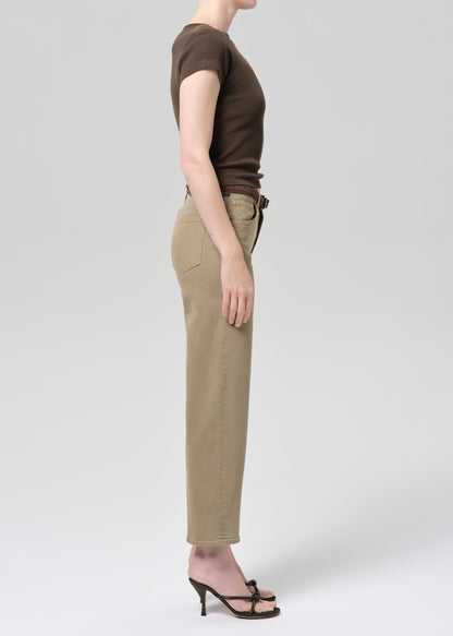 Person wearing a brown top and beige jeans on a grey background