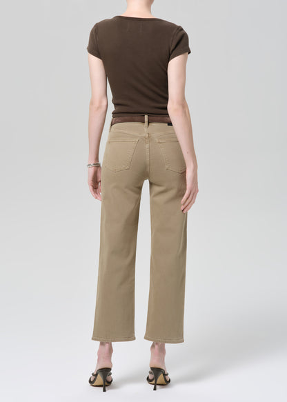 Person wearing a brown top and beige jeans on a grey background