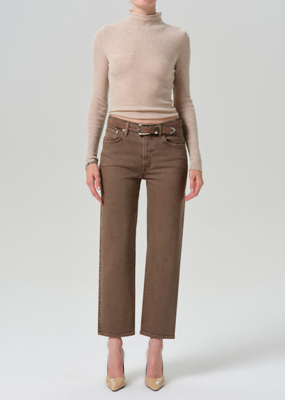A model wearing a beige ribbed turtleneck sweater and brown wide-leg cropped jeans with a matching belt, paired with beige heels, against a grey background.