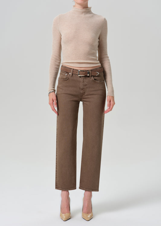 A model wearing a beige ribbed turtleneck sweater and brown wide-leg cropped jeans with a matching belt, paired with beige heels, against a grey background.