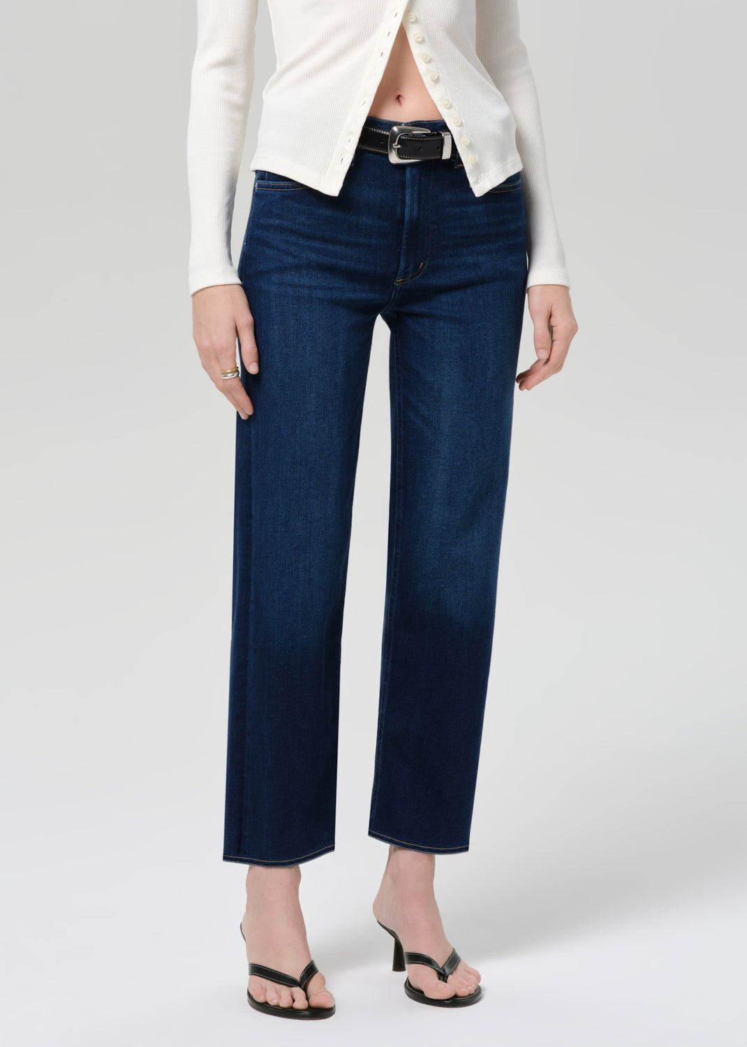Person wearing dark blue jeans and a white jacket on a plain background
