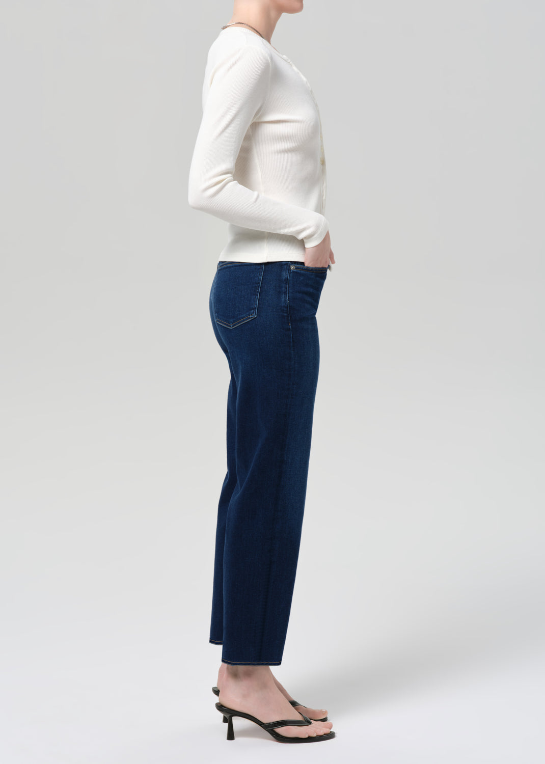 Person wearing a white sweater and dark blue jeans on a light gray background