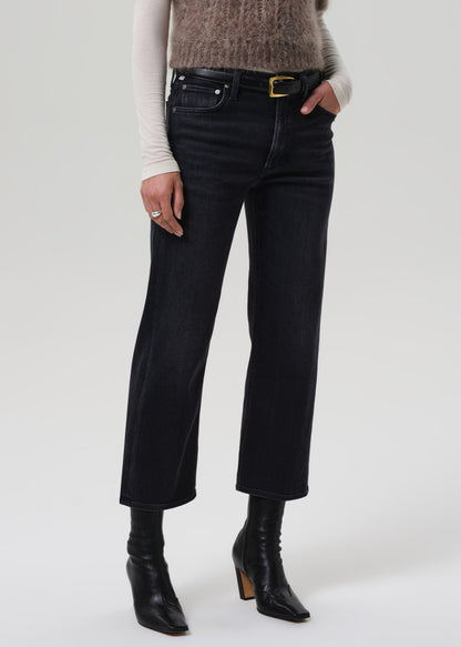 Person wearing a brown knitted sweater, white turtleneck, black jeans, and black boots on a light gray background