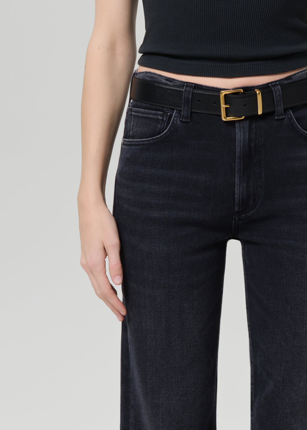 Person wearing a black sleeveless top and black jeans on a grey background