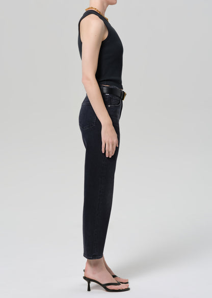 Person wearing a black sleeveless top and black jeans on a grey background