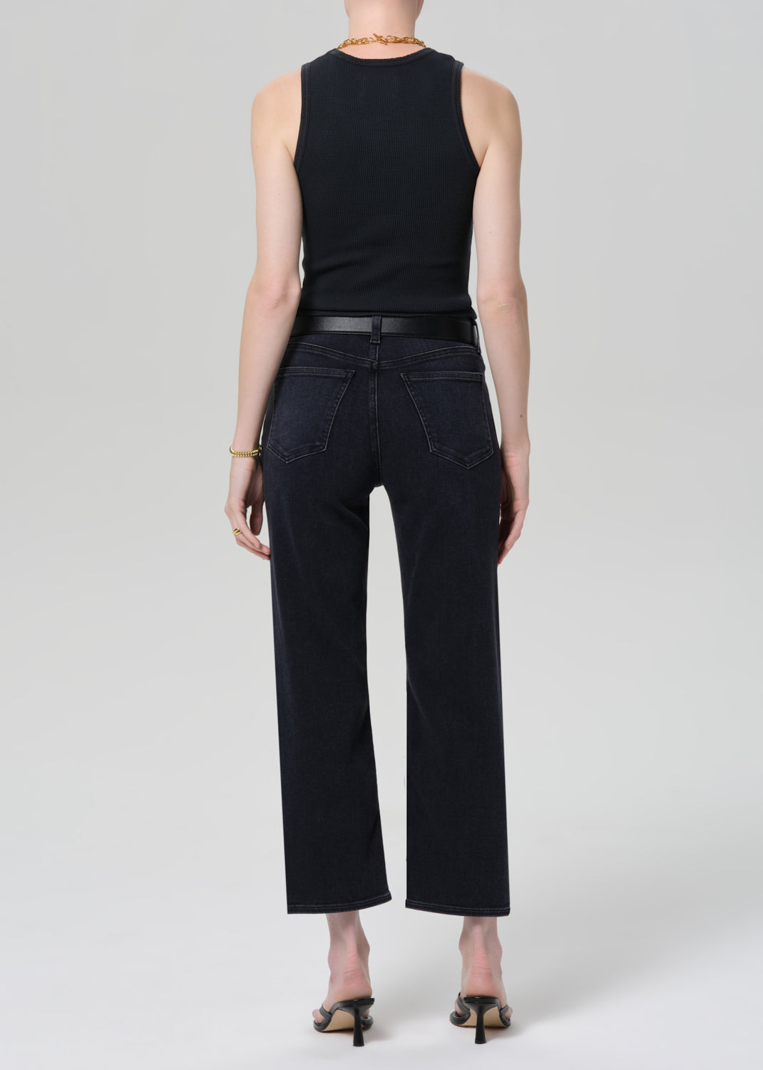 Person wearing a black sleeveless top and black jeans on a grey background