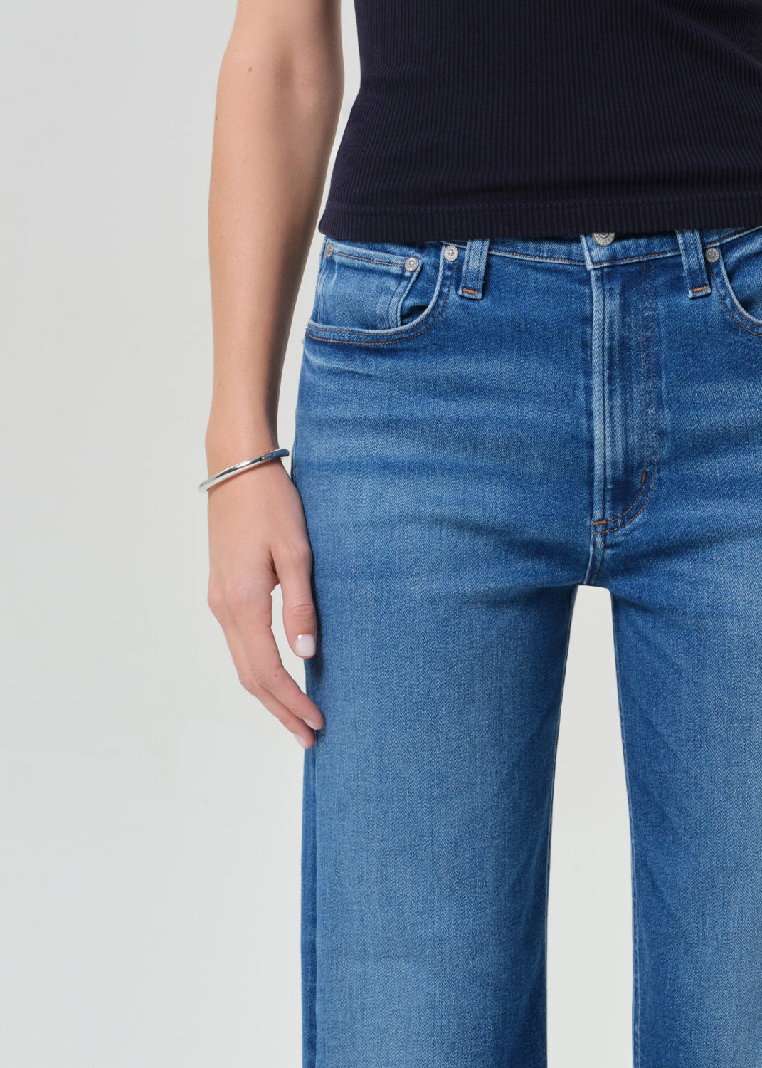 Person wearing a navy sleeveless top and blue jeans on a grey background