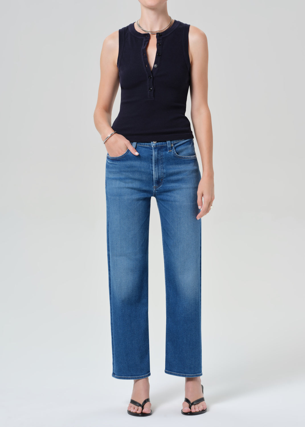 Person wearing a navy sleeveless top and blue jeans on a grey background