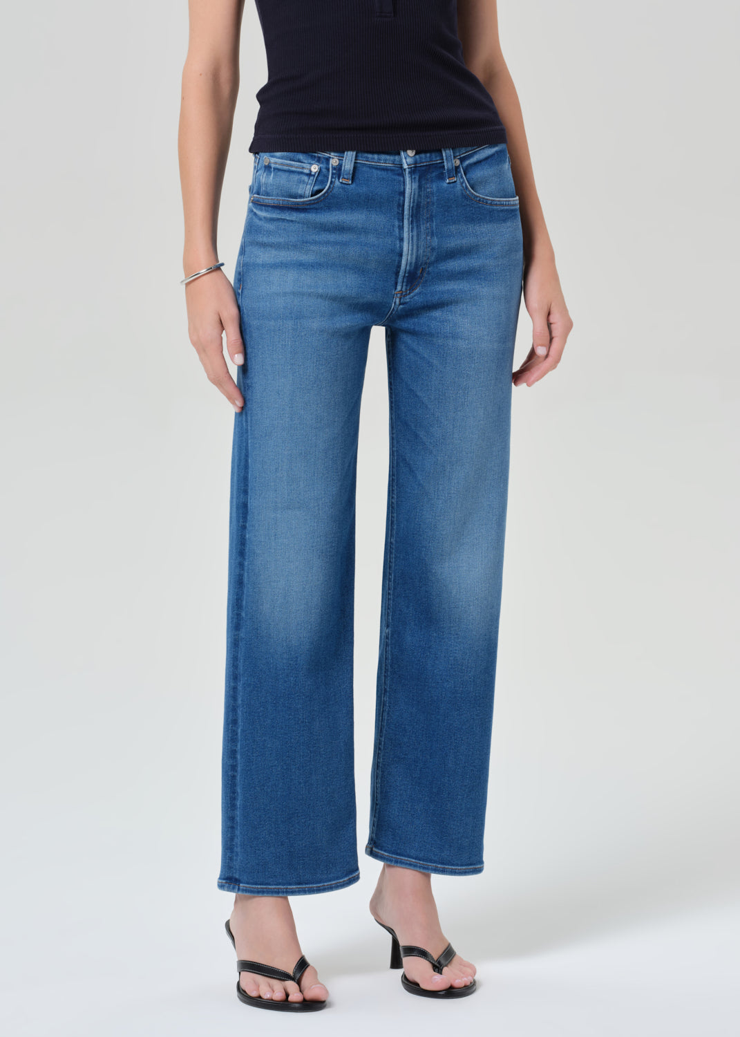 Person wearing a navy sleeveless top and blue jeans on a grey background