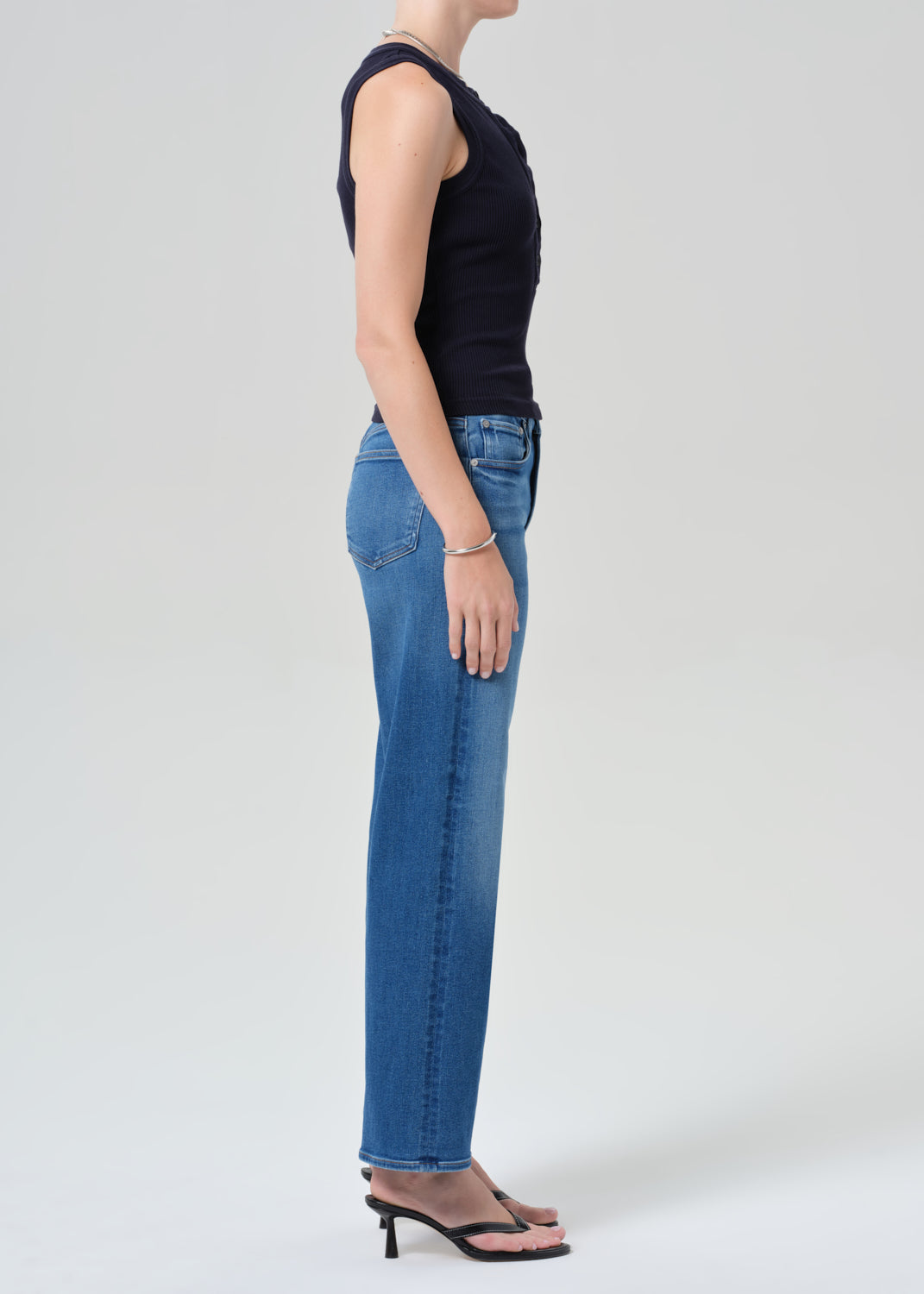 Person wearing a navy sleeveless top and blue jeans on a grey background