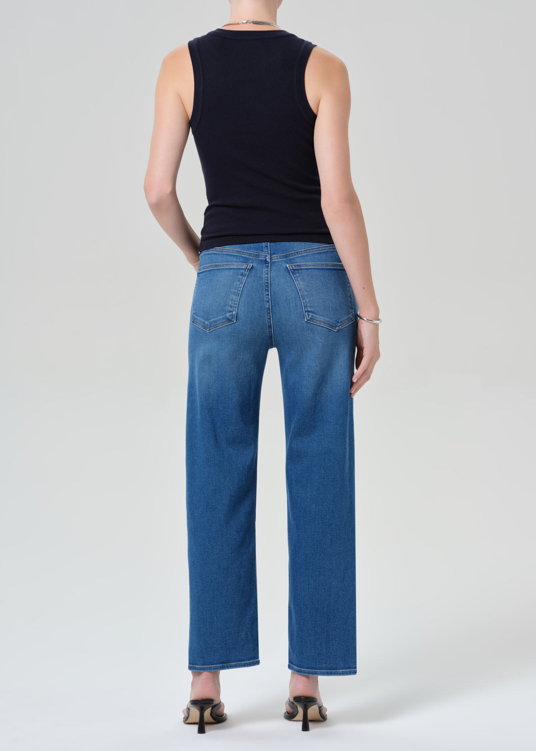 Person wearing a navy sleeveless top and blue jeans on a grey background