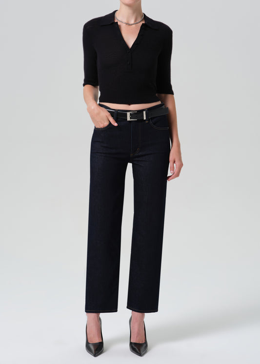 Person wearing a black polo and dark blue jeans on a grey background