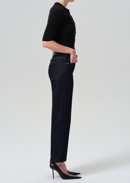 Person wearing a black polo and dark blue jeans on a grey background