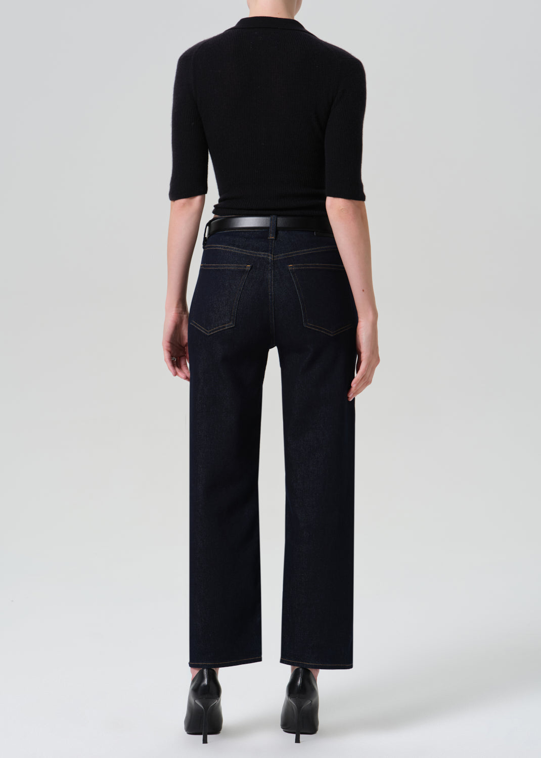 Person wearing a black polo and dark blue jeans on a grey background