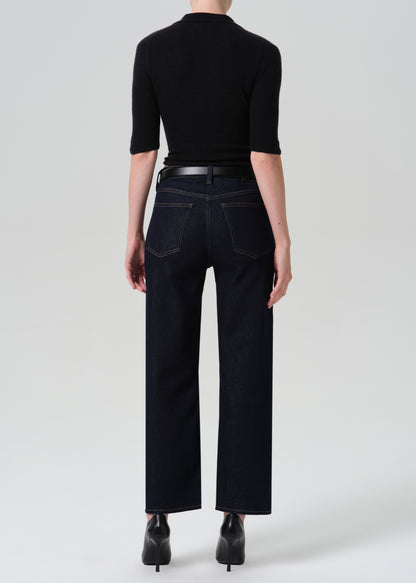 Person wearing a black polo and dark blue jeans on a grey background