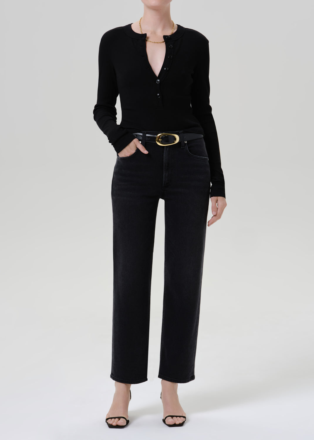 Person wearing a black long sleeve henley top with black straight leg jeans on a grey background