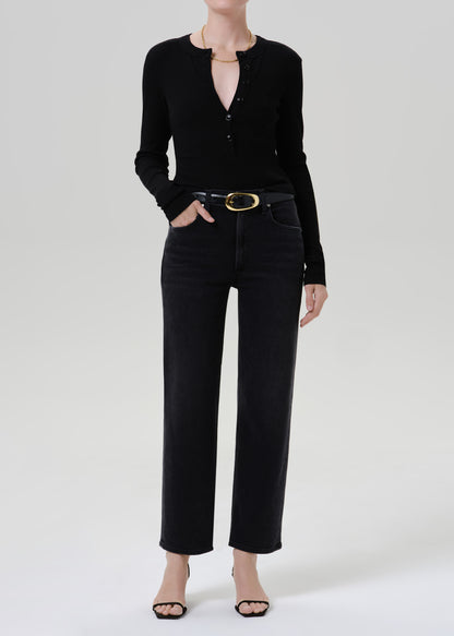 Person wearing a black long sleeve henley top with black straight leg jeans on a grey background